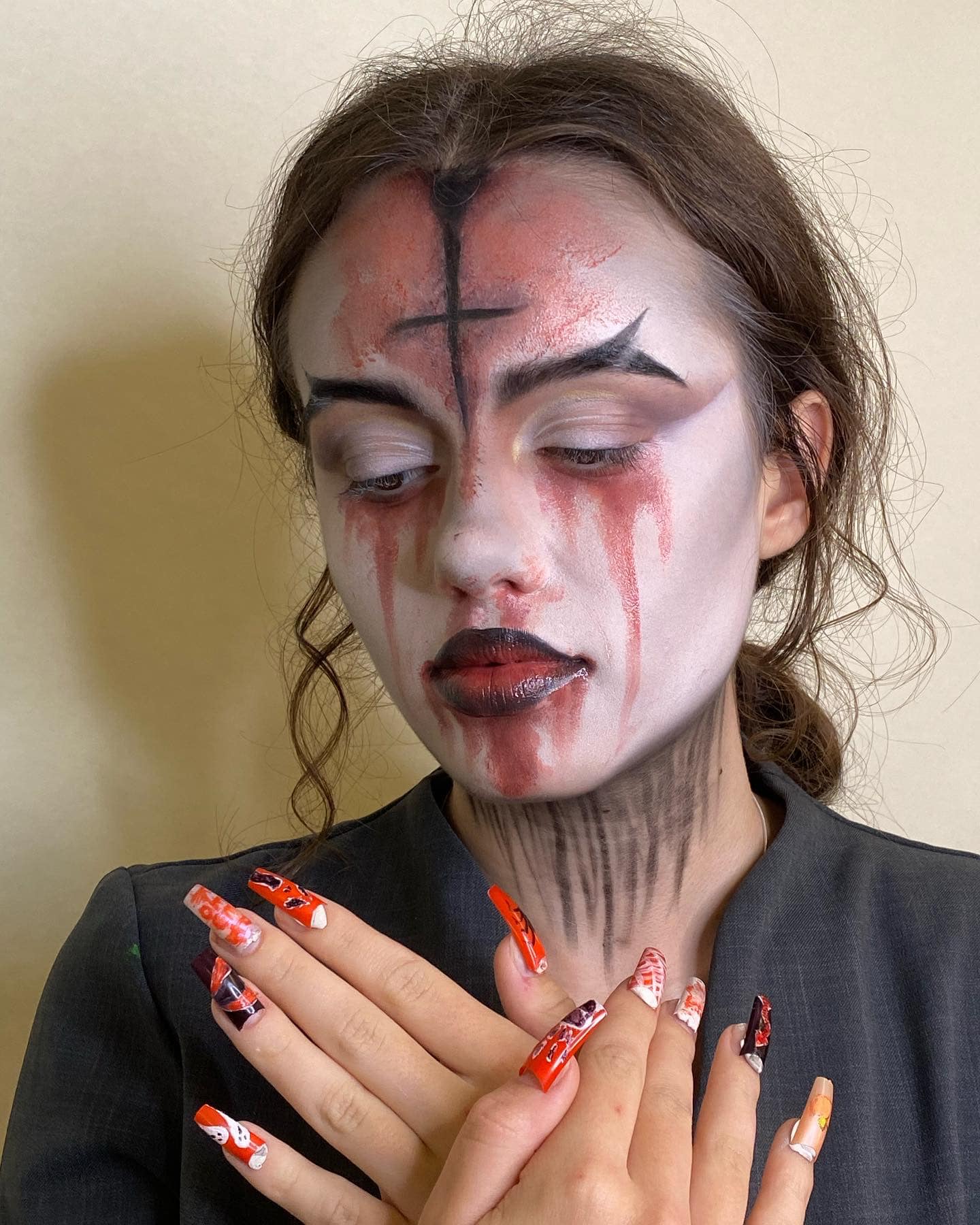 Theatrical makeup with pale base, red detailing, and dark lip.