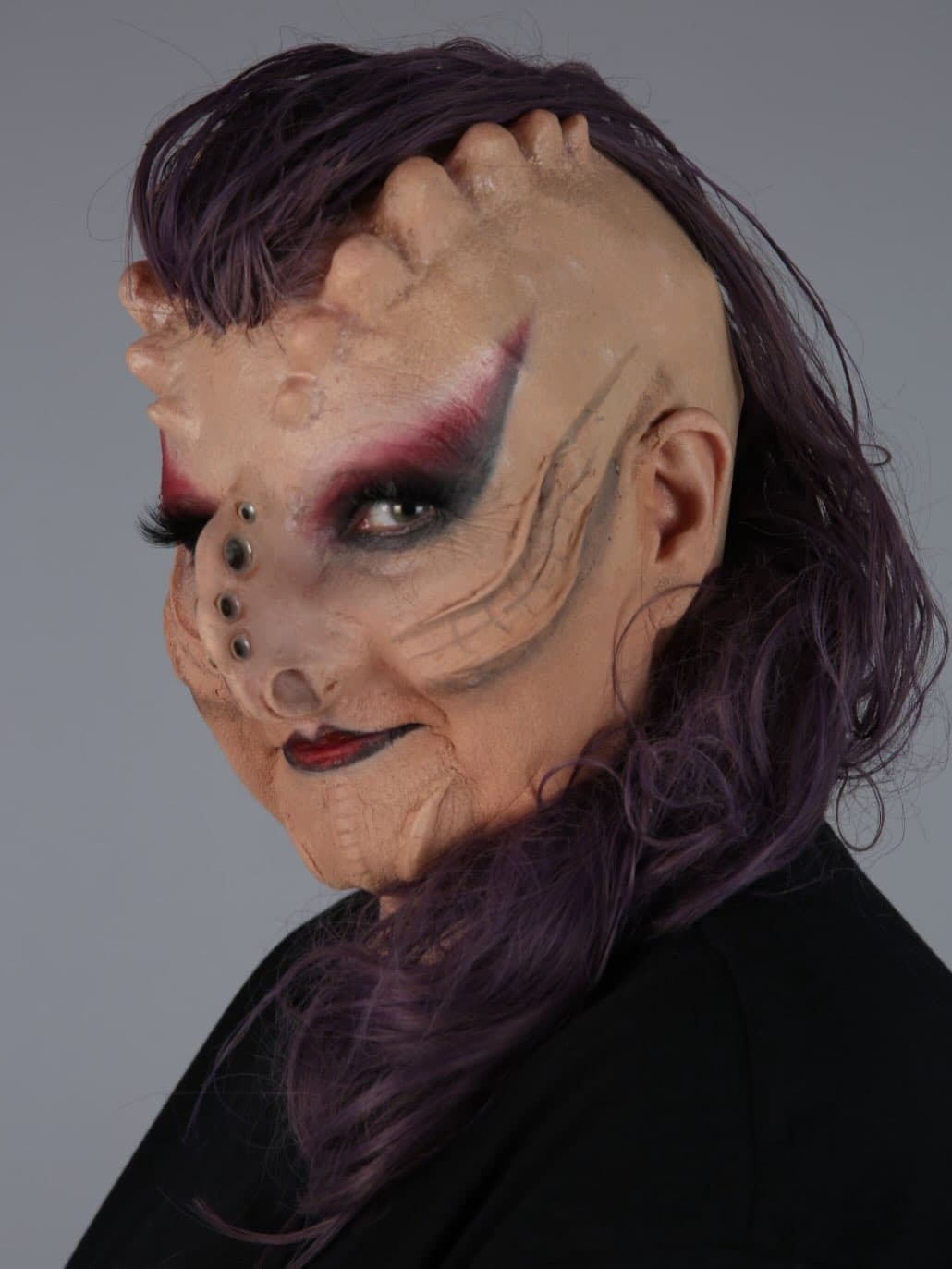 Special effects creature makeup with sculptural prosthetics and purple hair.